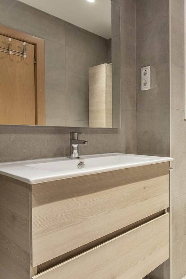 Mueble de almacenamiento para baño en tono madera bajo un gran espejo