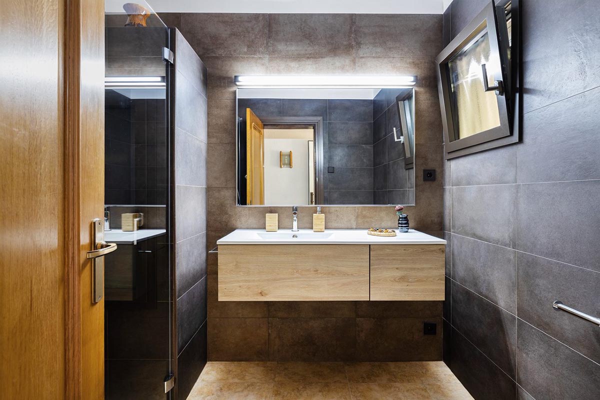 Baño reformado con azulejos grises, parquet y lavamanos en tono madera
