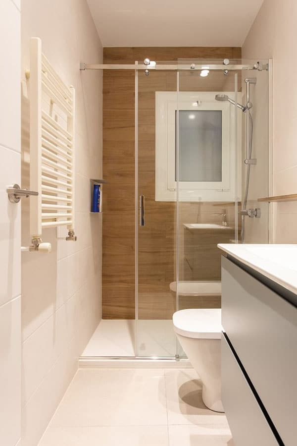 Baño reformado con ducha abierta y toallero eléctrico