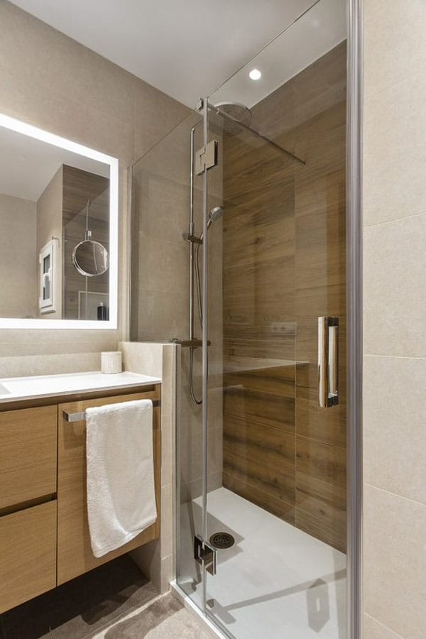 Baño reformado con colores madera y gran espejo en blanco