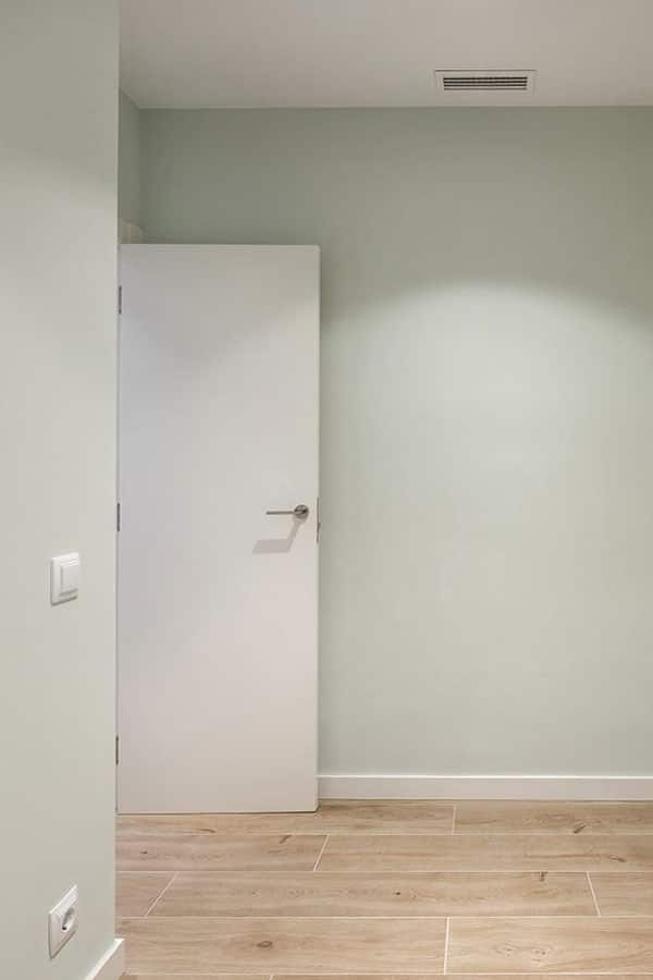 Estancia vacía con pared en tono verdoso y puerta blanca