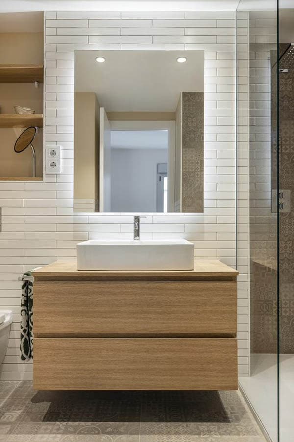 Mueble de almacenamiento para baño en tono madera bajo un espejo