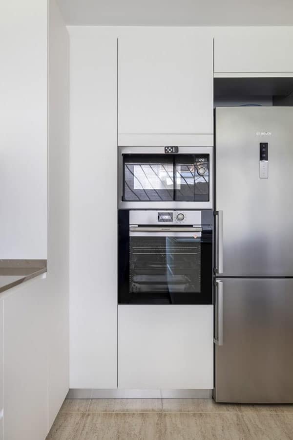 Nevera, horno y microondas integrados como parte del mobiliario blanco de cocina