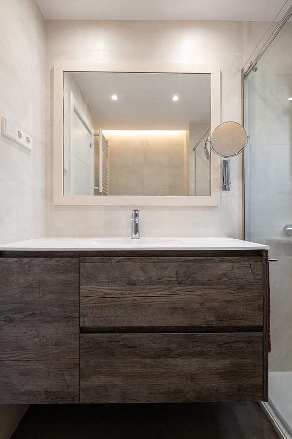 Vista frontal de un baño con mueble de madera oscura y espejos