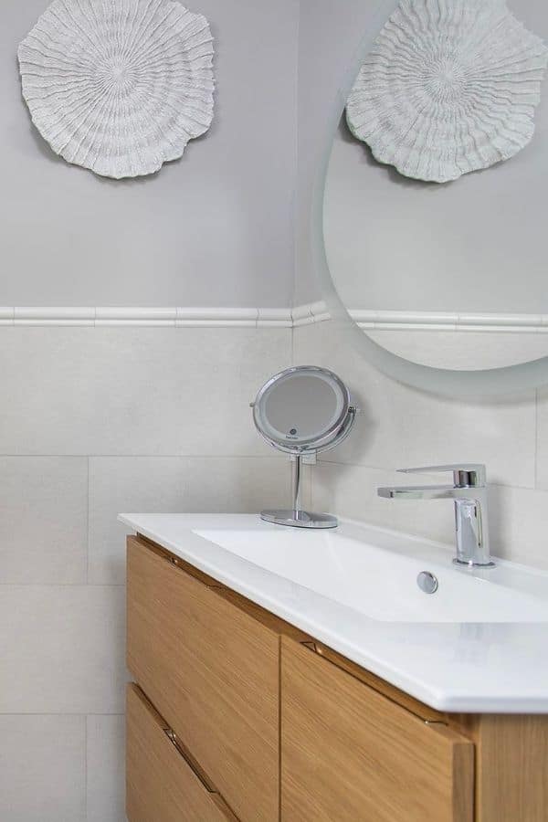 Baño con pica larga en blanco, espejos redondos y mueble de almacenamiento en madera